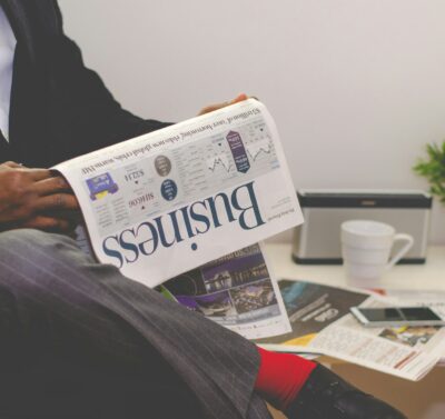 Pronar biznesi që lexon gazetën “Business” ndërsa planifikon strategjinë e tij financiare