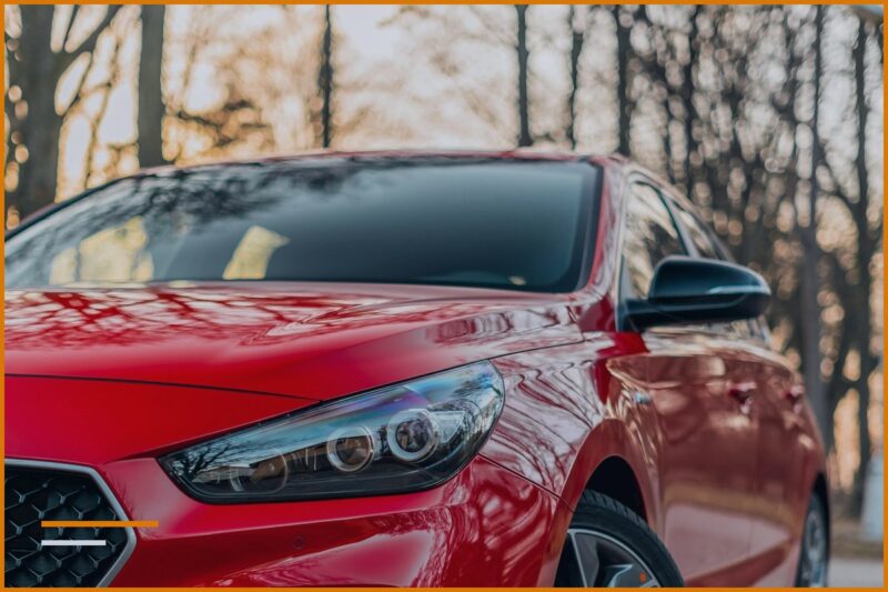 Auto rossa moderna e compatta parcheggiata all’esterno, vista frontale, senza targhe né contrassegni visibili.