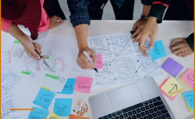 Mani che tracciano screenshot su post-it accanto a un portatile, a illustrare l'attività di un'azienda informatica.