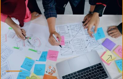 Hands marking up screenshots on sticky notes next to a laptop, illustrating the work of an IT business.