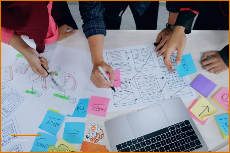 Hands marking up screenshots on sticky notes next to a laptop, illustrating the work of an IT business.