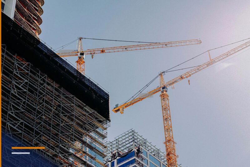 Dy vinça kullë portokalli mbi një ndërtesë në ndërtim e sipër, parë nga poshtë, me skelat e fasadës në plan të parë