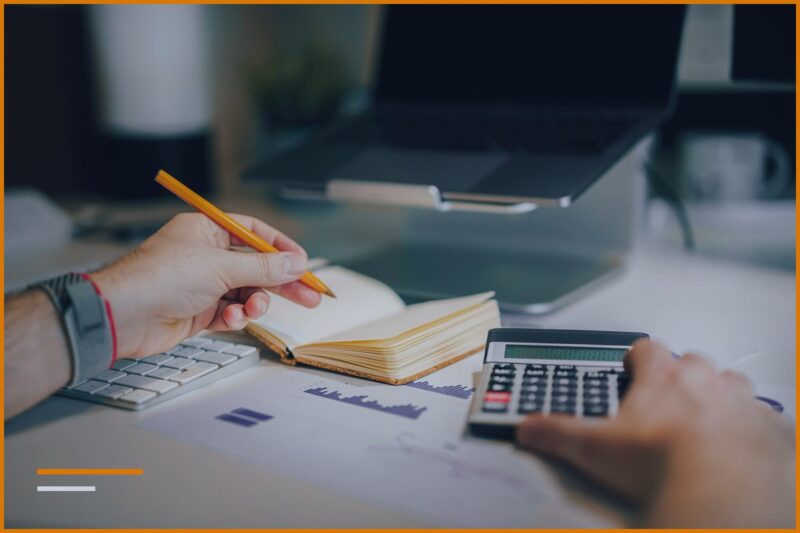 Hands holding a pencil over a notepad next to a calculator, calculating the days in the report.