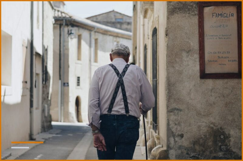 An elderly man with a cane walks along an Italian alleyway, pension Albania Italy