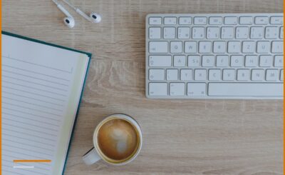 An open notepad, a keyboard, and a cup of coffee on a wooden desk.