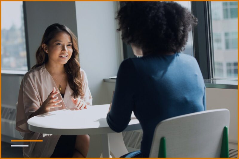 Due professionisti stanno parlando faccia a faccia seduti a un tavolo da lavoro.